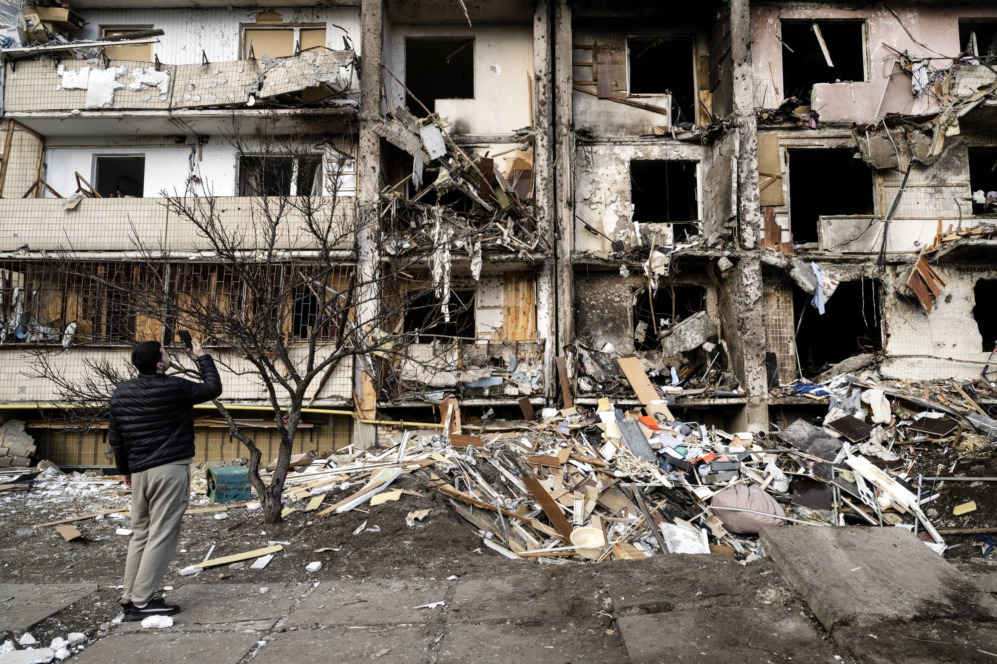 Ukrainians survey debris after a residential building was hit by missiles in the country’s capital of Kyiv on Feb. 25. As Ukrainians deal with the devastation of the Russian attacks in their homeland, many are also encountering a confounding and almost surreal backlash from family members in Russia, who refuse to believe that Russian soldiers could bomb innocent people, or even that a war is taking place at all. | LYNSEY ADDARIO / THE NEW YORK TIMES
