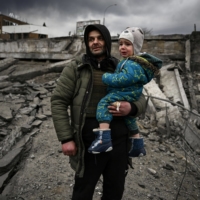 A man carries his son as they flee the city of Irpin, northwest of Kyiv, on Monday. | AFP-JIJI