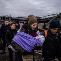A woman carrying her baby crosses a destroyed bridge as they flee the city of Irpin, northwest of Kyiv, on Monday. | AFP-JIJI