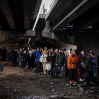Evacuees stand under a destroyed bridge as they flee the city of Irpin, northwest of Kyiv, on Monday. Ukraine dismissed Moscow\'s offer to set up humanitarian corridors from several bombarded cities on Monday after it emerged some routes would lead refugees into Russia or Belarus. | AFP-JIJI