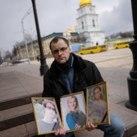 Serhiy Perebyinis holds portraits of his wife, Tetiana, and children Mykyta, 18, and Alisa, 9, who were killed by Russian mortar fire as they tried to evacuate two days earlier, in Kyiv, on Wednesday. | LYNSEY ADDARIO/THE NEW YORK TIMES



