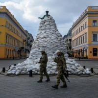 Ukrainian soldiers patrol near a monument covered with sand bags for protection against Russian attack in the city of Odessa on Thursday. | REUTERS