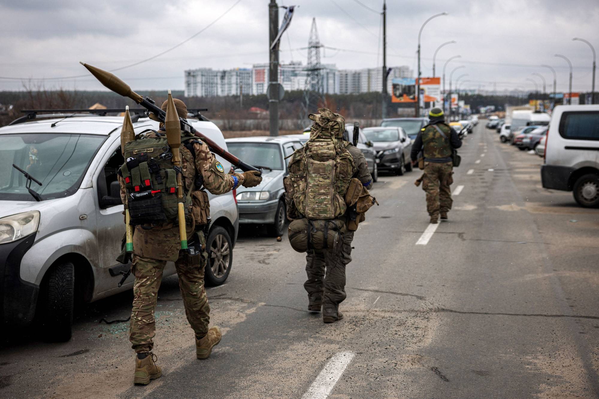 Ukrainian servicemen carry rocket-propelled grenades and sniper rifles as they walk toward the city of Irpin, northwest of Kyiv, on Sunday. | AFP-JIJI