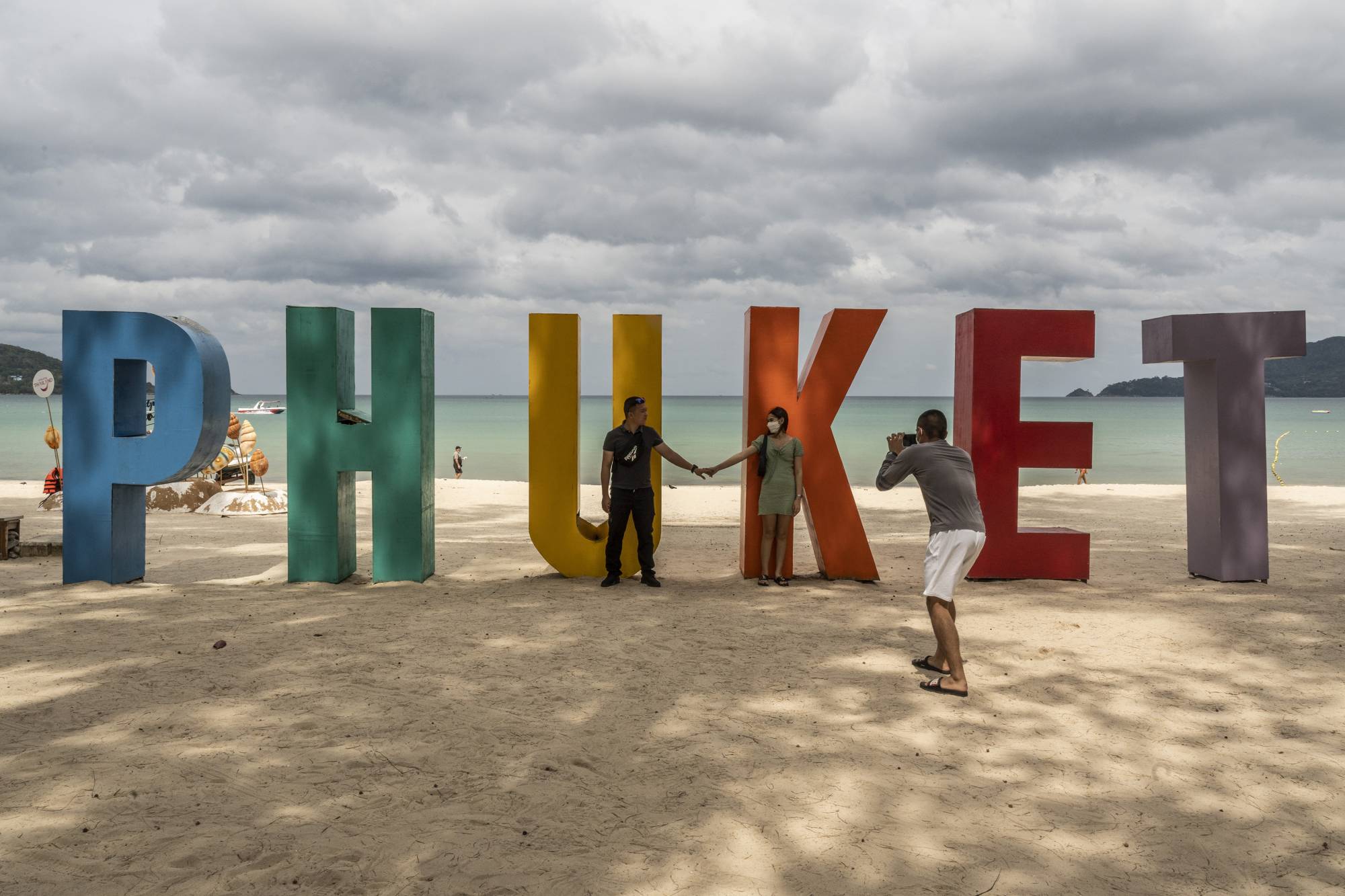 Visitors pose for photos on Phuket Island in Thailand, on Feb. 27. To visit Phuket Island, international tourists need to submit a “Thailand Pass,” which requires uploading vaccination records, hotel reservations and proof of health insurance. | Adam Dean / The New York Times