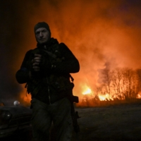 A Ukrainian serviceman stands in front of a burning warehouse amid shelling in Kyiv on Thursday. | AFP-JIJI