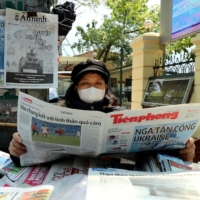 A woman reads a Vietnamese newspaper featuring front page coverage of the Russian invasion of Ukraine at her stall in Hanoi on Feb. 25. | AFP-JIJI