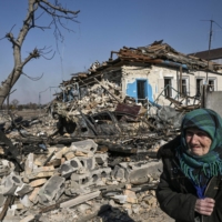 An elderly woman walks past a destroyed house in the village of Krasylivka, east of Kyiv, on Sunday. | AFP-JIJI