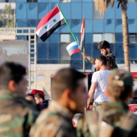 A Syrian soldier waves Russian and Syrian flags during a protest against air strikes in Damascus, Syria, on April 14, 2018. | REUTERS