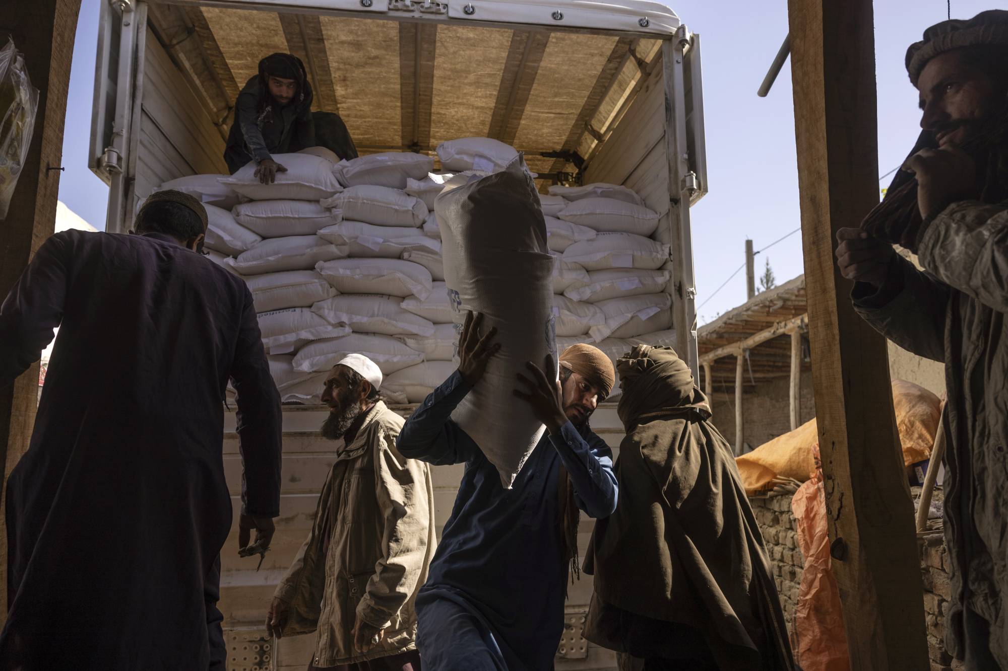 Laborers unload sacks of flour from a World Food Program convoy that traveled from Kabul to Afghanistan’s Tagab district, on Oct. 27. Aid workers warn that a humanitarian crisis has already been exacerbated by the war in Ukraine, making it more difficult to feed the roughly 23 million Afghans. | Victor J. Blue / The New York Times