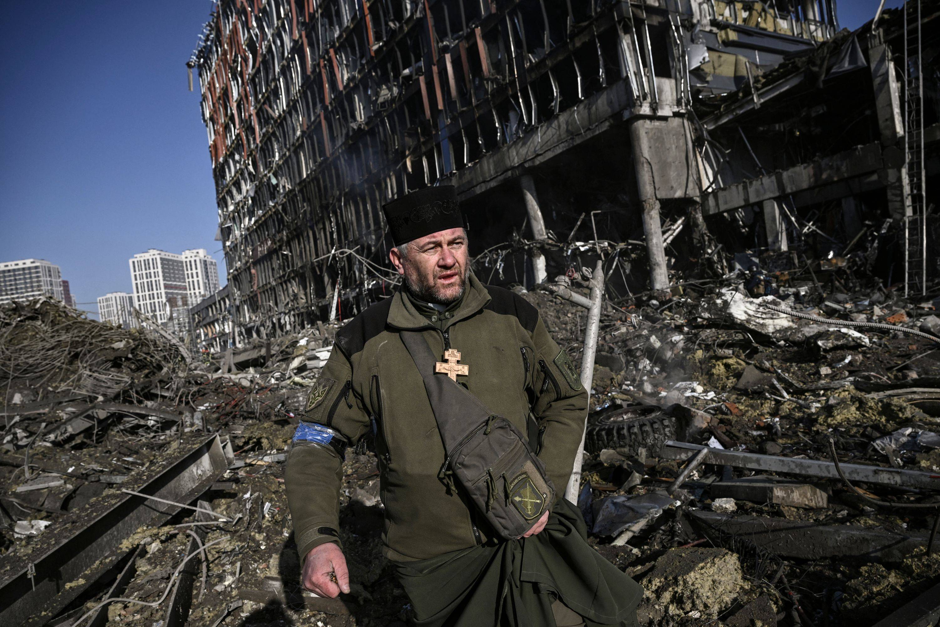 Ukrainian Army chaplain Mikola Madenski walks through debris outside the destroyed Retroville shopping mall in a residential district of Kyiv on Monday. | AFP-JIJI