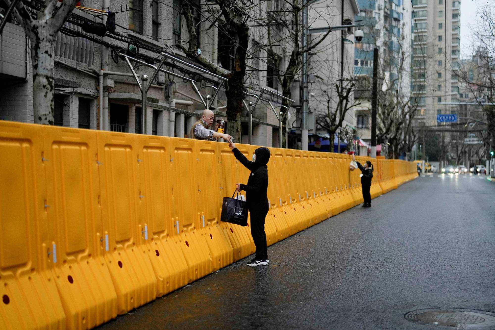 People pass food to residents over the barriers of an area under COVID-19 lockdown in Shanghai, China | Reuters