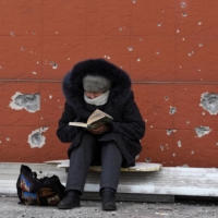 A resident of Mariupol, Ukraine, reads a book near a building damaged in the course of the Ukraine-Russia conflict in the southern port city on Sunday. | REUTERS