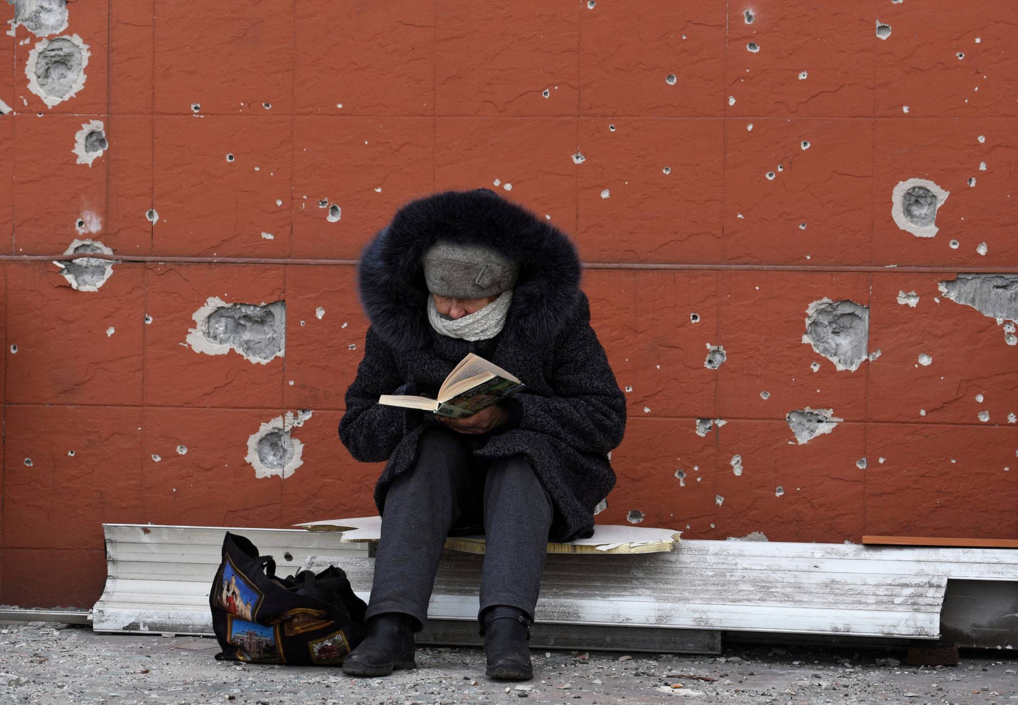 A resident of Mariupol, Ukraine, reads a book near a building damaged in the course of the Ukraine-Russia conflict in the southern port city on Sunday. | REUTERS