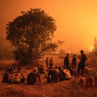 Residents gather to watch over the wildfire and wait to support firefighters outside the village of Kamatriades, on Evia island, Greece, in August. | BLOOMBERG