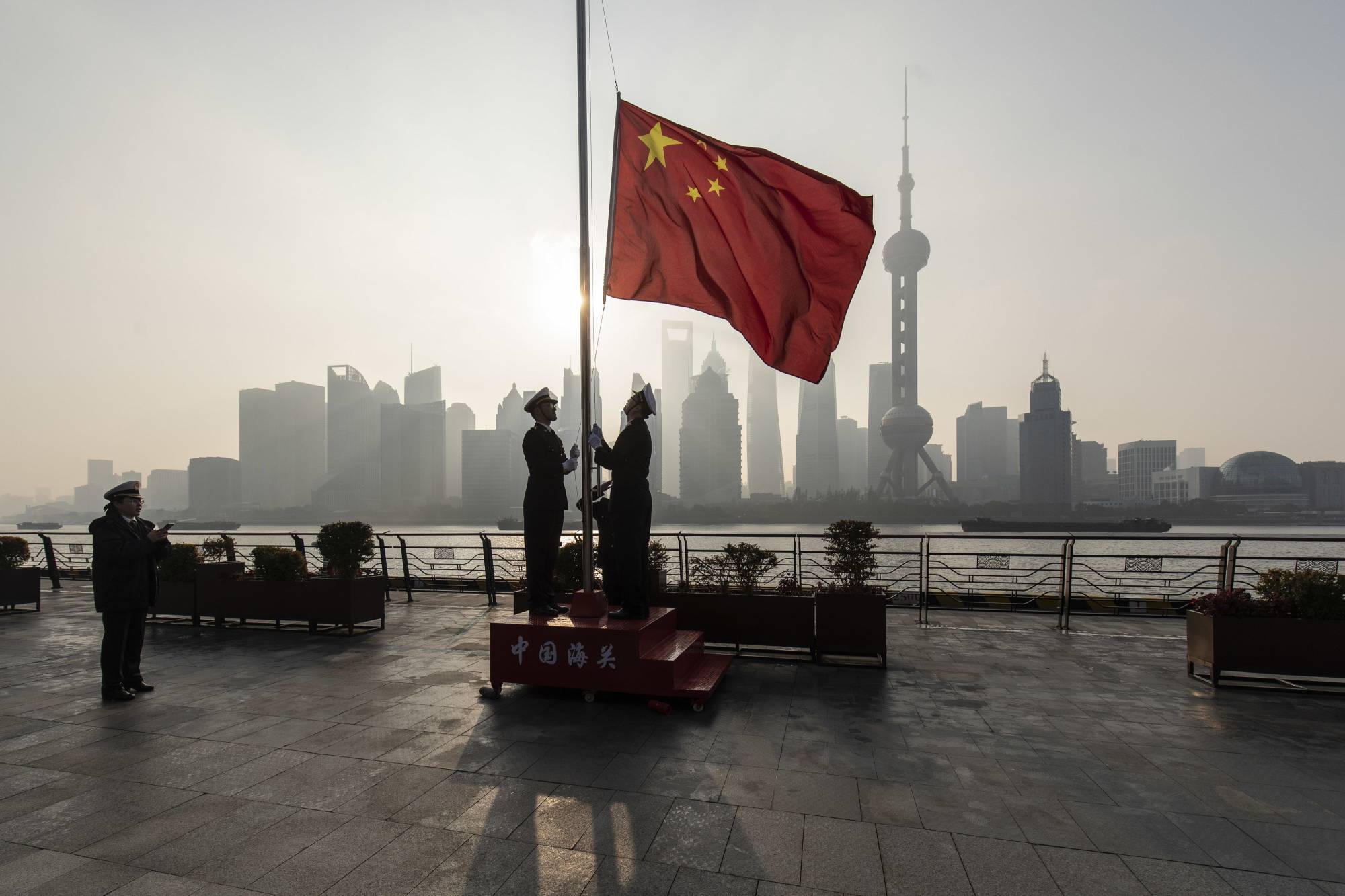 China Customs officers raise a Chinese flag at sunrise during a rehearsal for a flag-raising ceremony along the Bund, in front of buildings in the Lujiazui Financial District in Shanghai, in January. | Bloomberg 