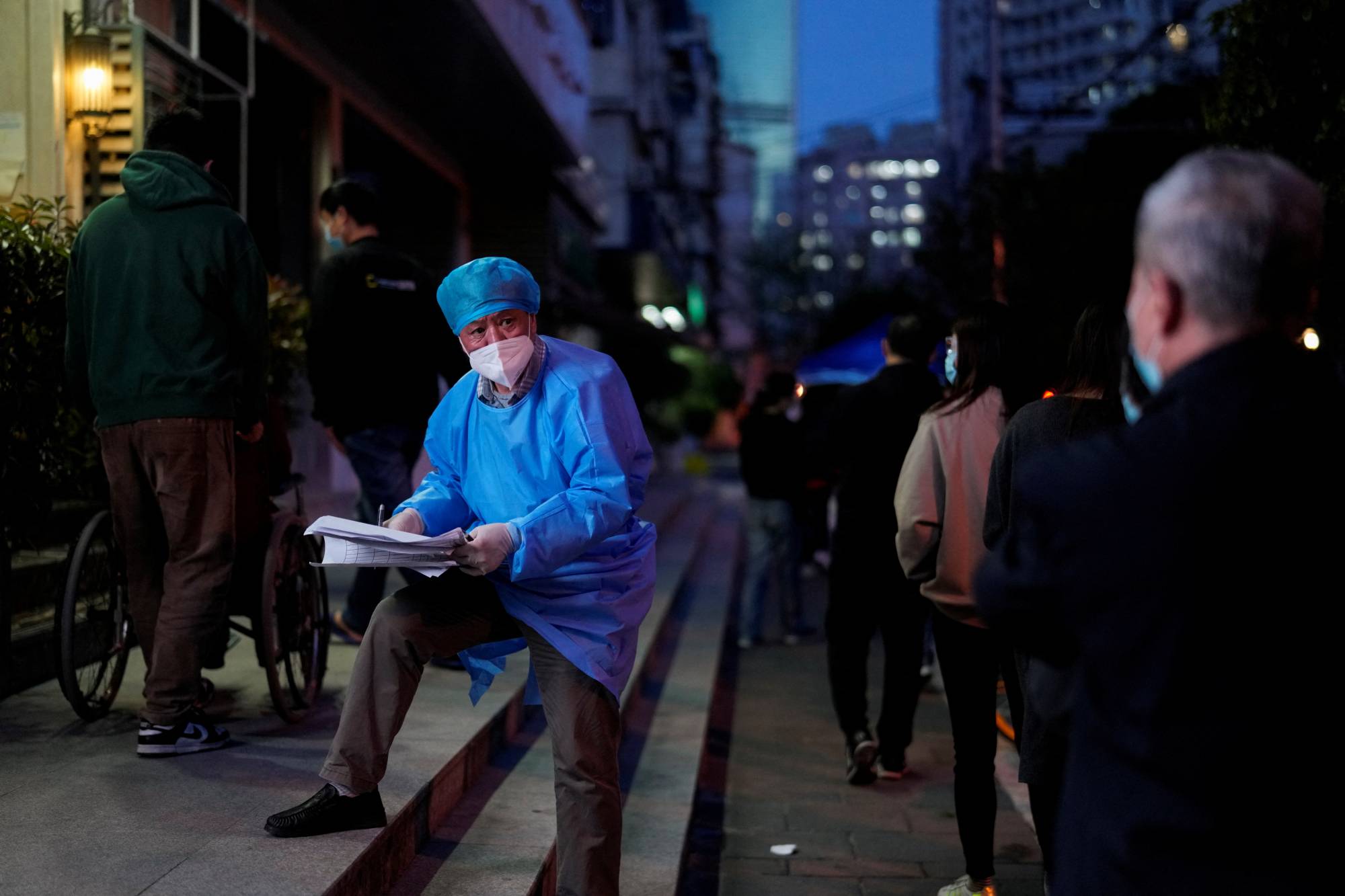 A worker in a protective suit directs residents lining up for nucleic acid test during a lockdown to curb the spread of COVID-19 in Shanghai on Saturday. | REUTERS