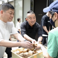 Yoshihiro Narisawa (left), owner and chef of Michelin-starred restaurant Narisawa in Tokyo, hands out onigiri rice balls for donors to support children in Ukraine on Monday. | KYODO
