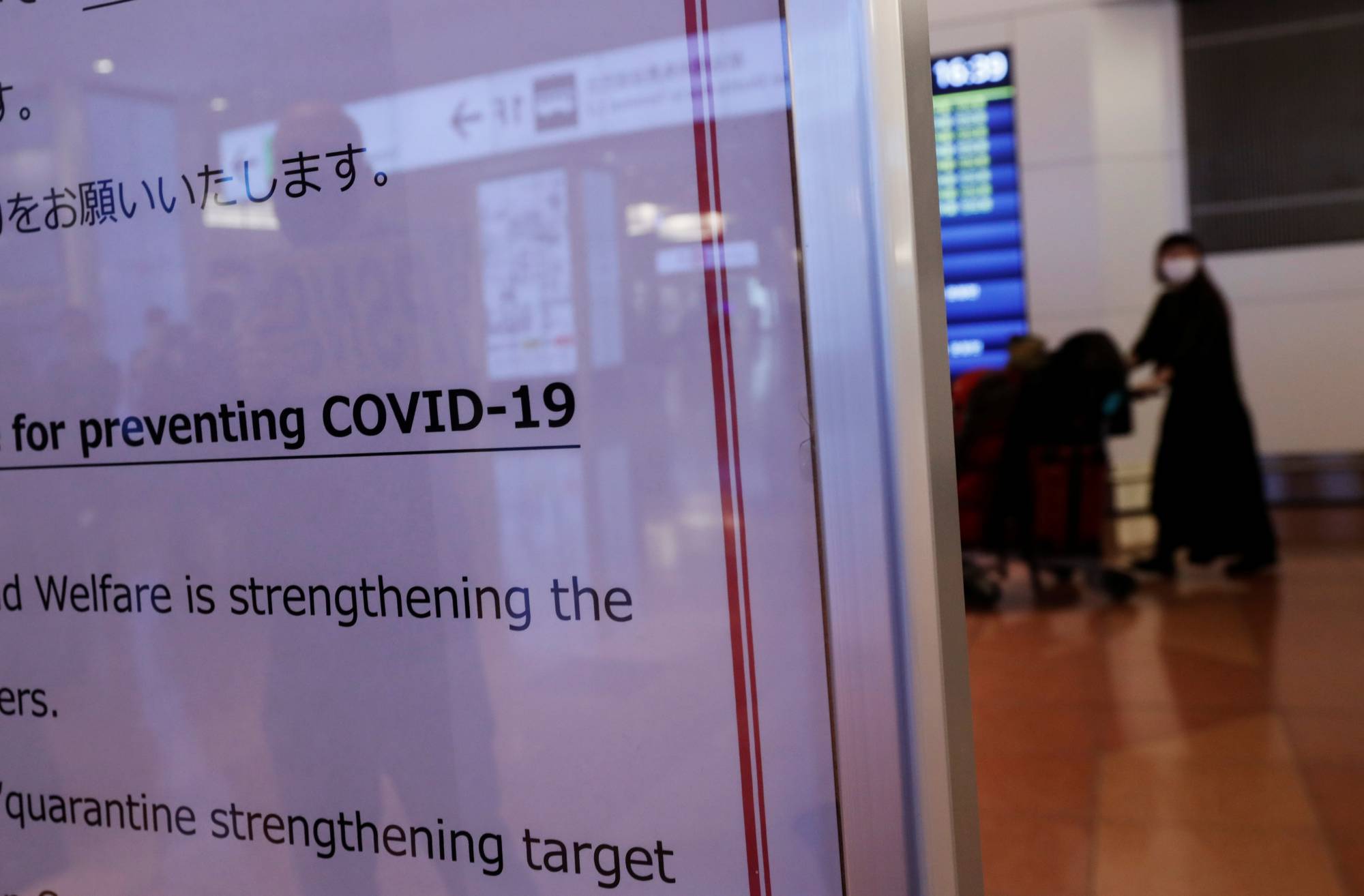 A passenger is seen behind a notice about COVID-19 measures at Tokyo's Haneda Airport.  | REUTERS