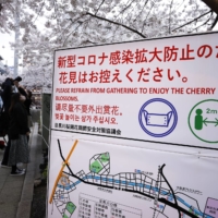 A COVID-19 awareness sign near cherry trees in full bloom along the Meguro River in Tokyo in March | BLOOMBERG