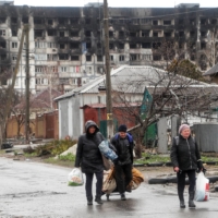 Local residents walk in front of a residential building damaged in the course of Russia\'s war on Ukraine in the southern port city of Mariupol, Ukraine, on Wednesday. | REUTERS