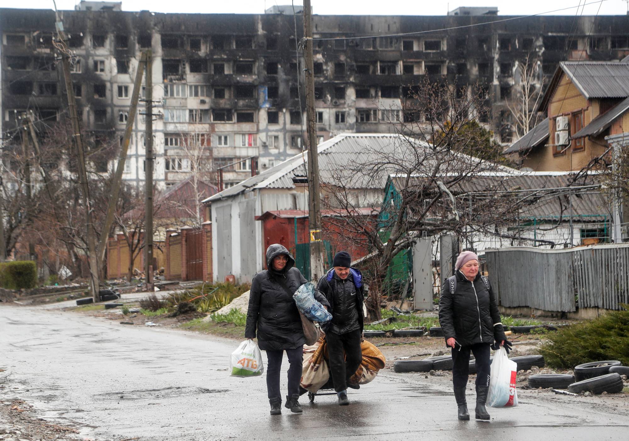 Local residents walk in front of a residential building damaged in the course of Russia's war on Ukraine in the southern port city of Mariupol, Ukraine, on Wednesday. | REUTERS