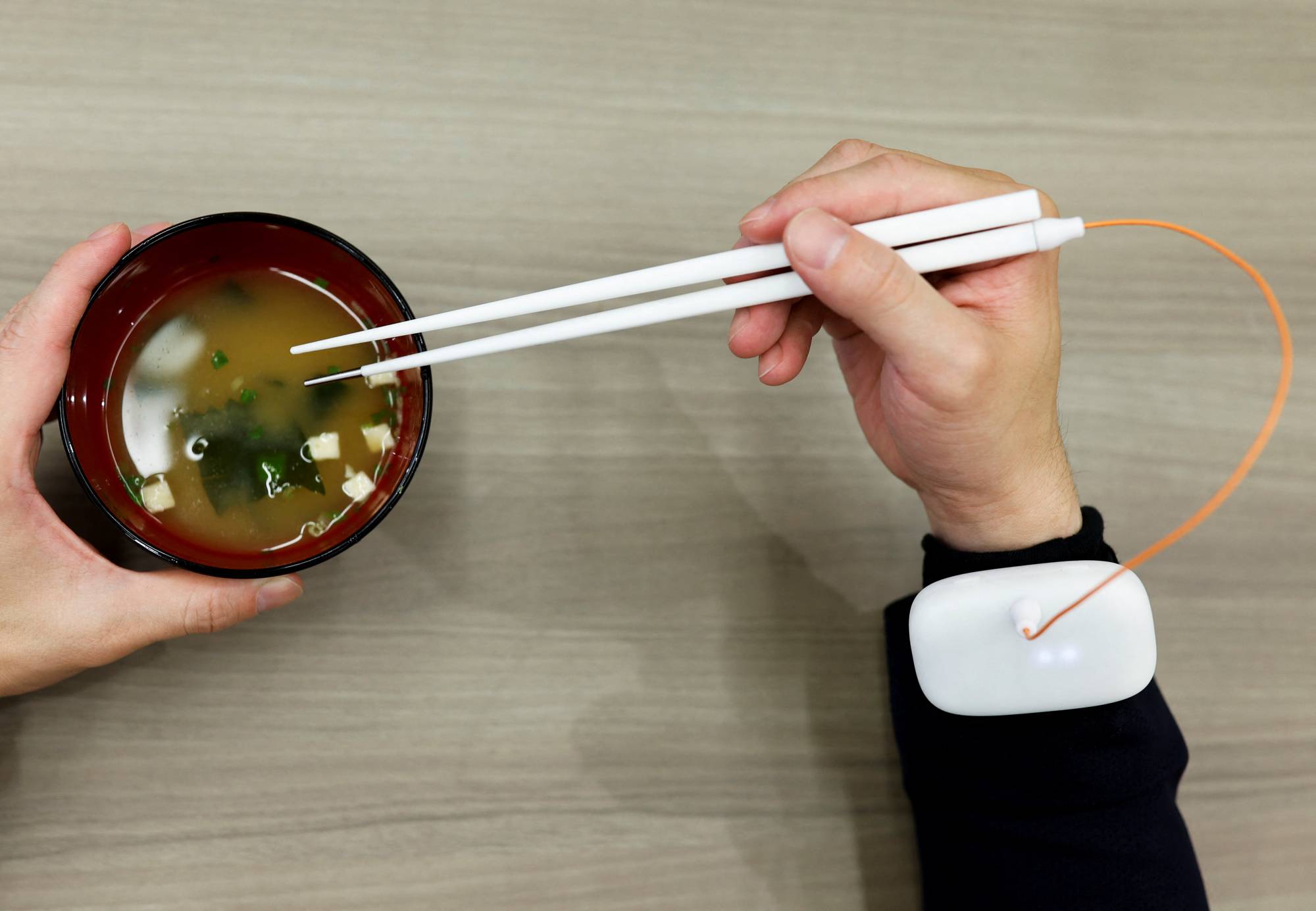 A Kirin Holdings Co. employee demonstrates chopsticks that can enhance the taste of food using an electrical stimulation waveform that was jointly developed by the company and Meiji University's School of Science and Technology Professor Homei Miyashita, in Tokyo on Friday. | REUTERS