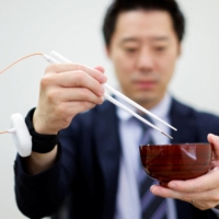 An employee of Kirin Holdings Co. demonstrates chopsticks that can enhance food taste using an electrical stimulation waveform in Tokyo on Friday. | REUTERS