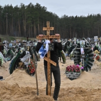 A communal worker sets a cross on a grave during a funeral at a cemetery in Irpin, Ukraine, on Tuesday. | AFP-JIJI