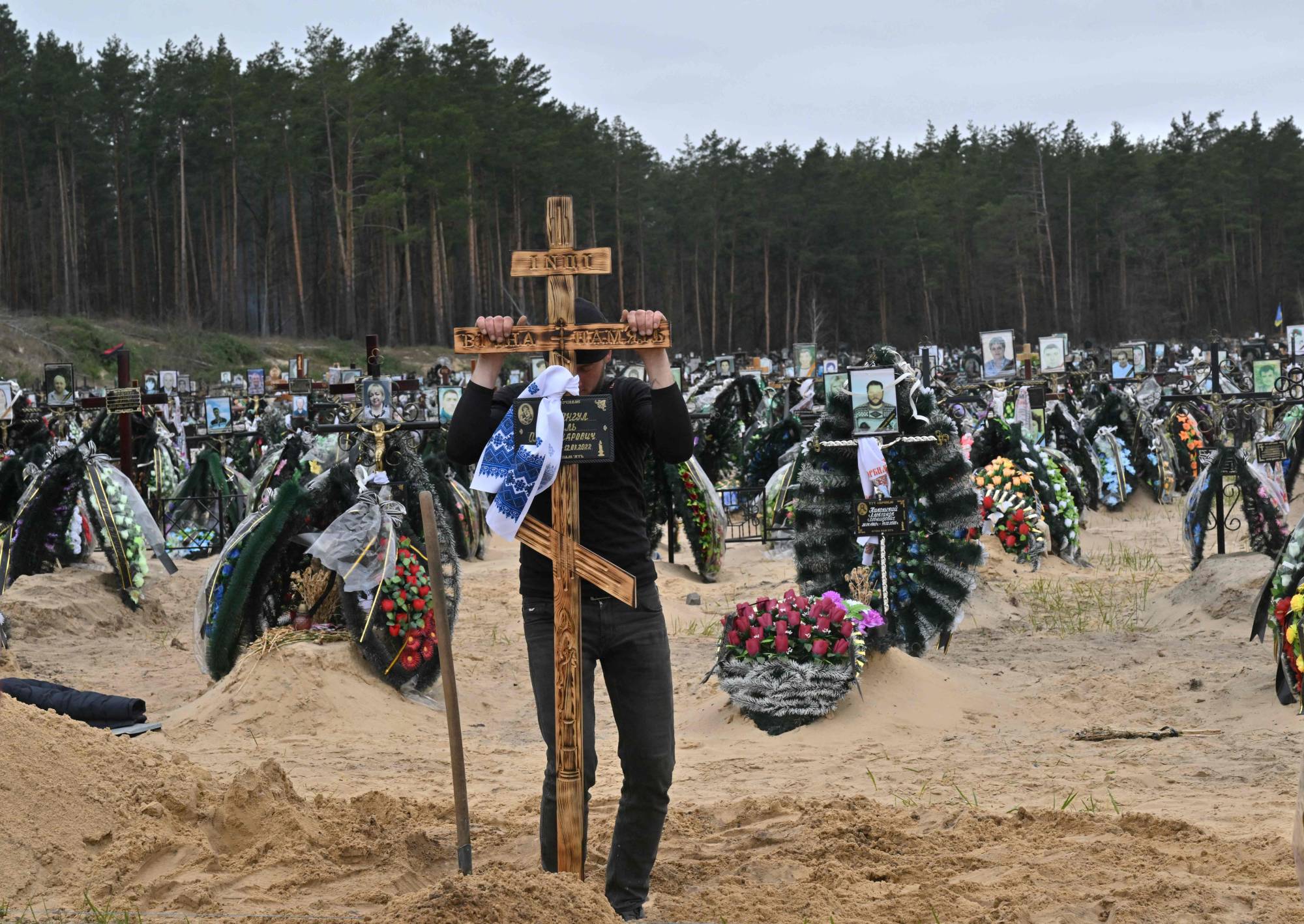 A communal worker sets a cross on a grave during a funeral at a cemetery in Irpin, Ukraine, on Tuesday. | AFP-JIJI