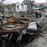 Residents walk amid debris of a charred Russian tank next to destroyed houses in the village of Zalissya, northeast of Kyiv, on Tuesday.  | AFP-JIJI