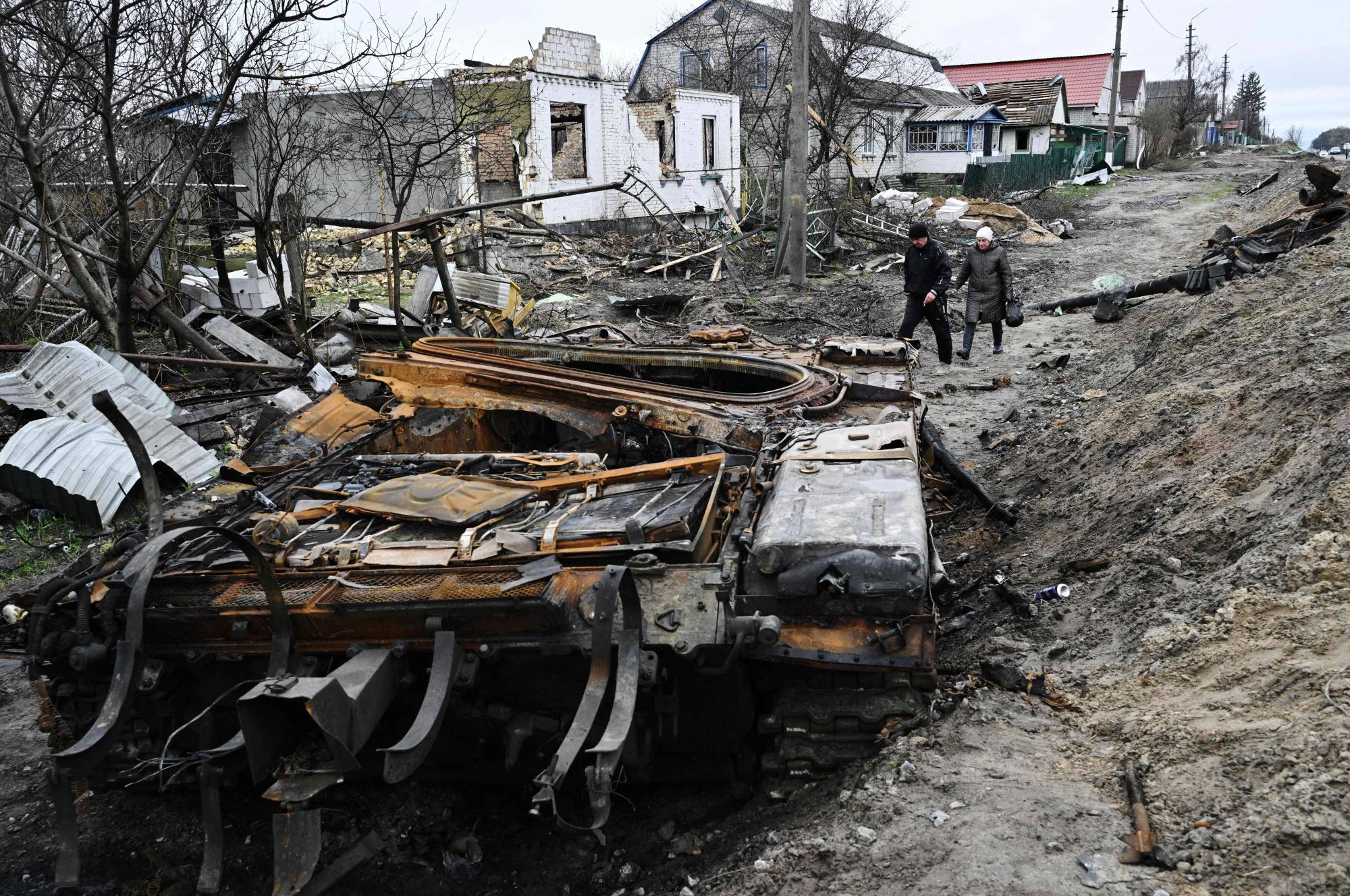 Residents walk amid debris of a charred Russian tank next to destroyed houses in the village of Zalissya, northeast of Kyiv, on Tuesday.  | AFP-Jiji