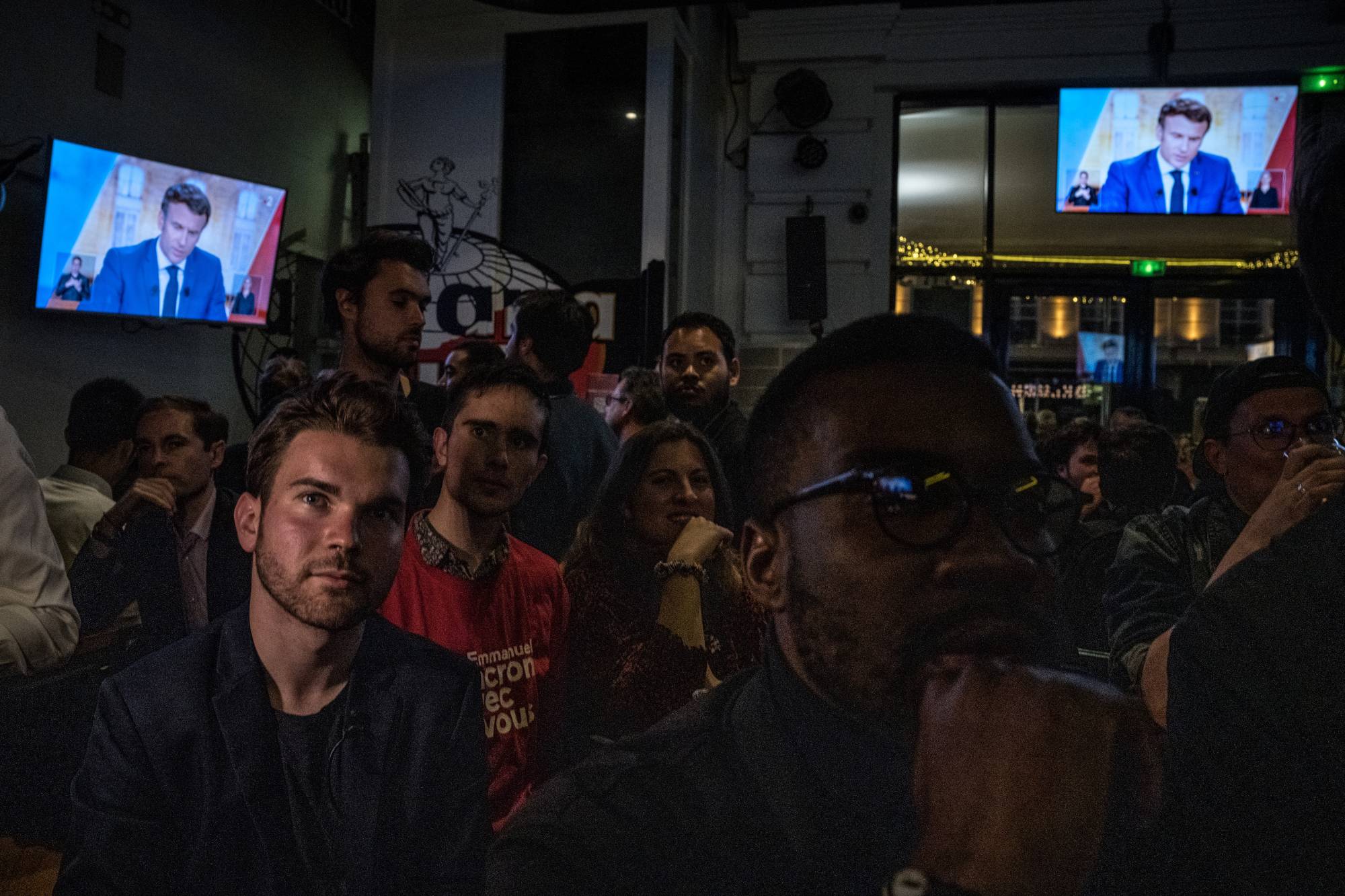 French President Emmanuel Macron is seen on television screens in a bar in Paris as people watch a presidential debate between Macron and Marine Le Pen on Wednesday. | Sergey Ponomarev / The New York Times