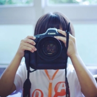 A child holds up a camera for a photography session at the Designing Artists Academy, which runs this year from Aug. 1 to 5.
