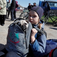 A child holds a dog as evacuees wait before boarding a bus to leave the southern port city of Mariupol, Ukraine, on Wednesday. | REUTERS