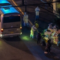 A health worker wearing personal protective equipment talks to the residents who are waiting to board a bus along a street during a COVID-19 lockdown in the Jing\'an district in Shanghai on Tuesday. | AFP-JIJI