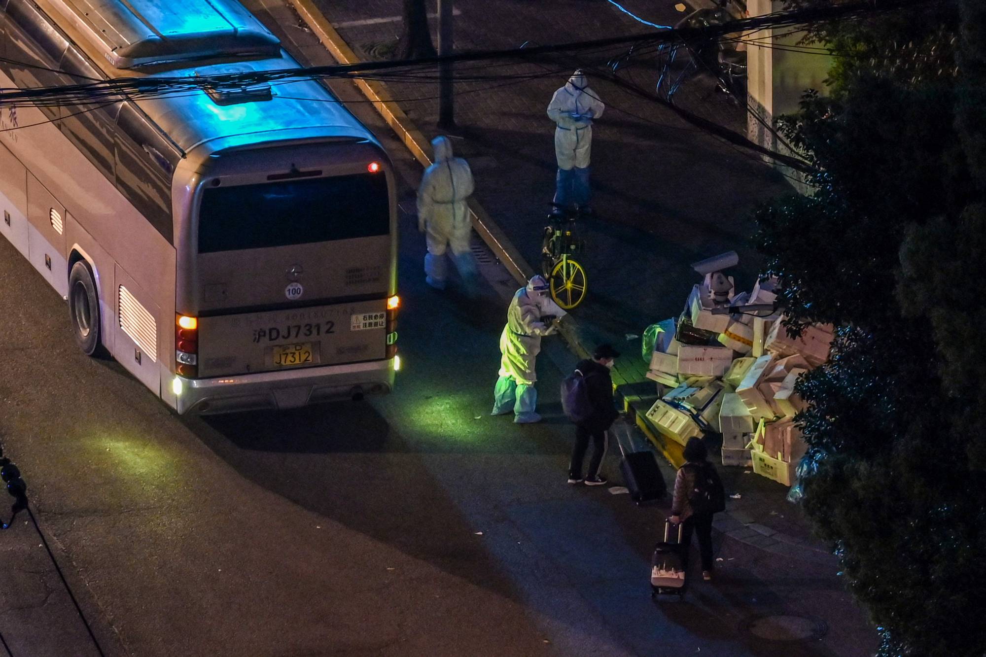 A health worker wearing personal protective equipment talks to the residents who are waiting to board a bus along a street during a COVID-19 lockdown in the Jing'an district in Shanghai on Tuesday. | AFP-JIJI