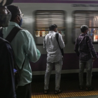 Passengers wait as a train arrives at Dadar railway train station in Mumbai in August 2021. | BLOOMBERG