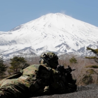 A member of the Self-Defense Force’s Amphibious Rapid Deployment Brigade takes a position as Mount Fuji stands in the background during joint exercises with the U.S. Marine Corps in Gotemba, Shizuoka Prefecture, on March 15. | REUTERS