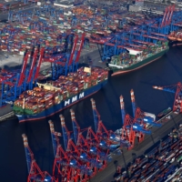 Cargo ships are loaded at a container terminal in Hamburg on Wednesday. Economists think the global economy will expand more slowly than predicted three months ago. | REUTERS