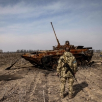 Ukrainian soldiers stand by a burnt Russian tank on the outskirts of Kyiv, on March 31.  | AFP-JIJI