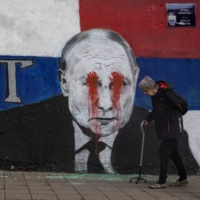 A person walks next to a mural of Russian President Vladimir Putin, which has been vandalized with red spray paint and the word \"war\" written instead of the original text reading: \"Brother,\" following Russia\'s invasion of Ukraine, in Belgrade, on Friday. | REUTERS