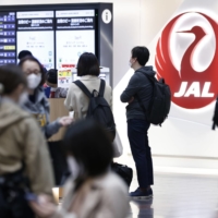Passengers wait in line to use Japan Airlines Co. self-service check-in machines at Haneda Airport on April 29. | BLOOMBERG