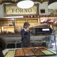 Freshly-baked loaves of bread and pizzas sit for sale inside the store of a bakery in Rome on March 9. Wheat futures have swung wildly as Russia\'s attack on Ukraine disrupts global food supplies. | BLOOMBERG