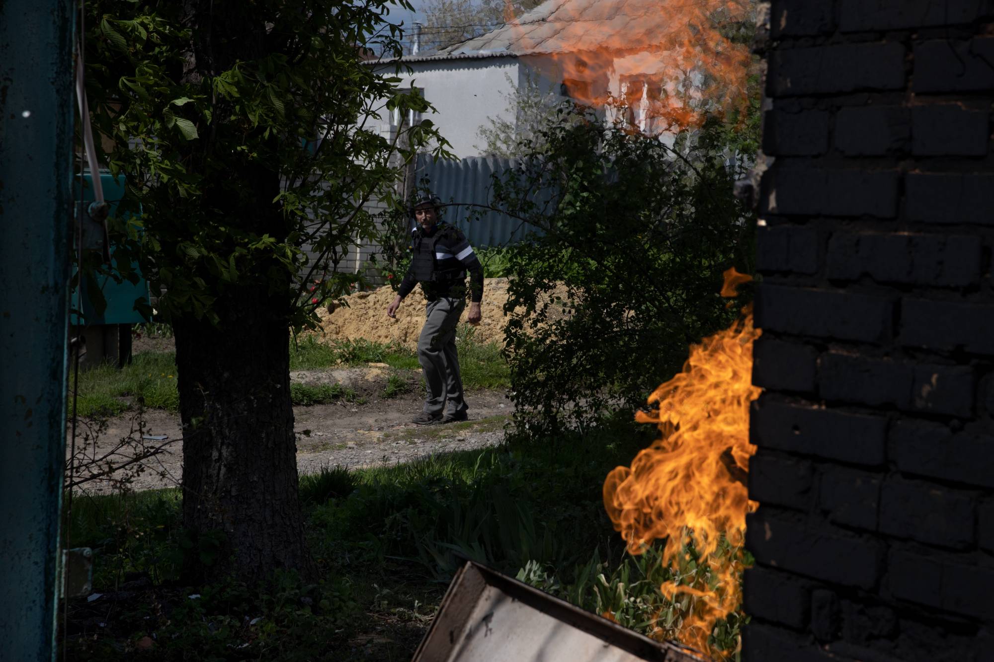 Oleg, a construction worker-turned-volunteer, walks by a burning house as he looks for residents to evacuate in Ruska Lozova, Ukraine, on Wednesday. | TYLER HICKS / THE NEW YORK TIMES