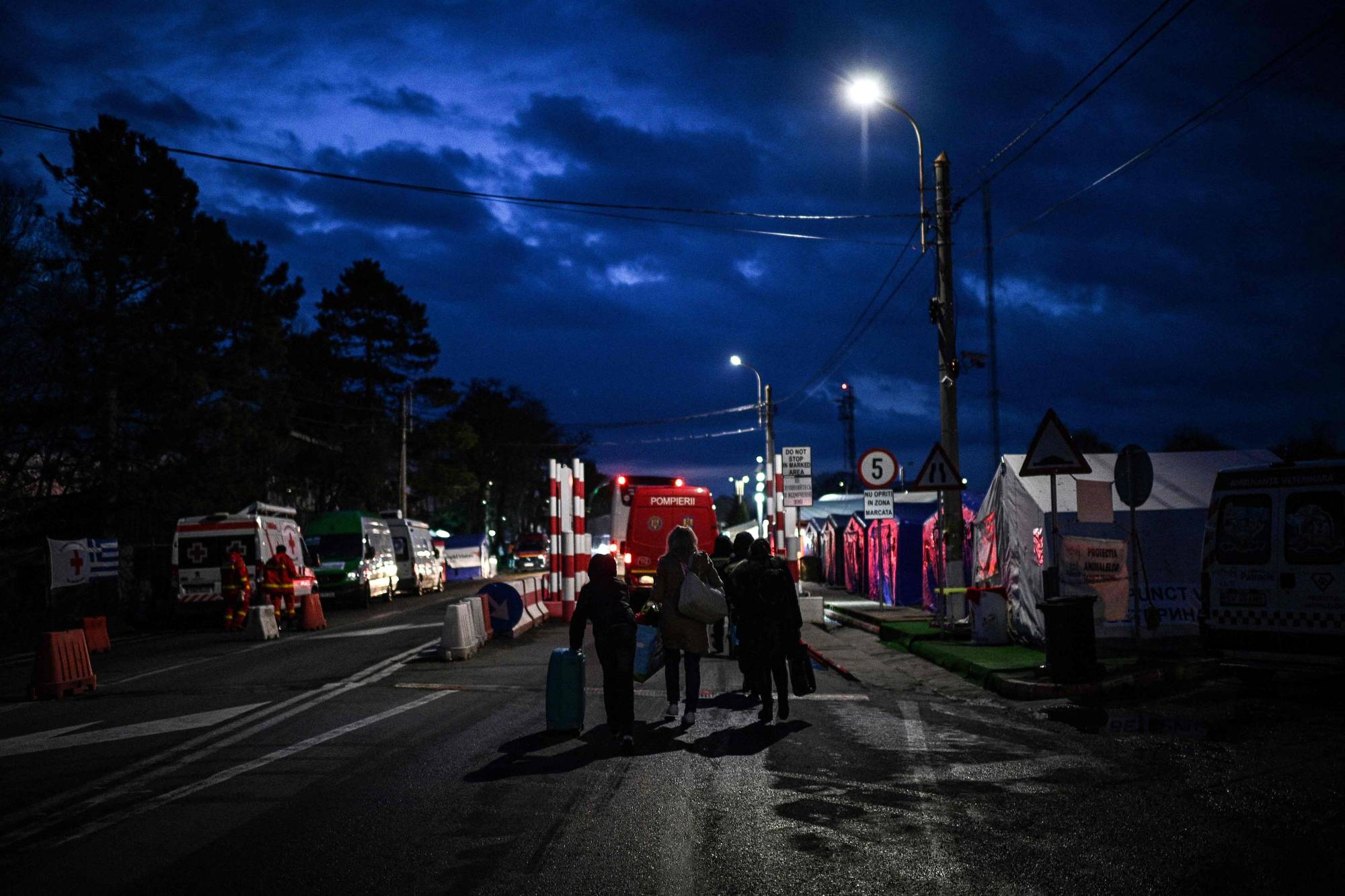 Ukrainian refugees pull their luggage past nongovernmental organization tents as they walk toward the Ukrainian-Romanian border on their way back to Ukraine, at the Siret border crossing in northeastern Romania on April 10. | AFP-JIJI