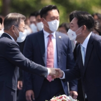 New South Korean President Yoon Suk-yeol shakes hands with former President Moon Jae-in upon his arrival at Yoon\'s inauguration ceremony at the National Assembly in Seoul on Tuesday.  | POOL / VIA REUTERS