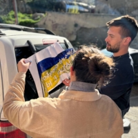 Maria Belkina and her partner Kirill Zhivoi, co-founders of Volunteers Tbilisi, a group which helps refugees from Ukraine, stick a sign with the Ukrainian flag onto a vehicle in Tbilisi, Georgia, on April 15. | MARIA BELKINA / VIA REUTERS