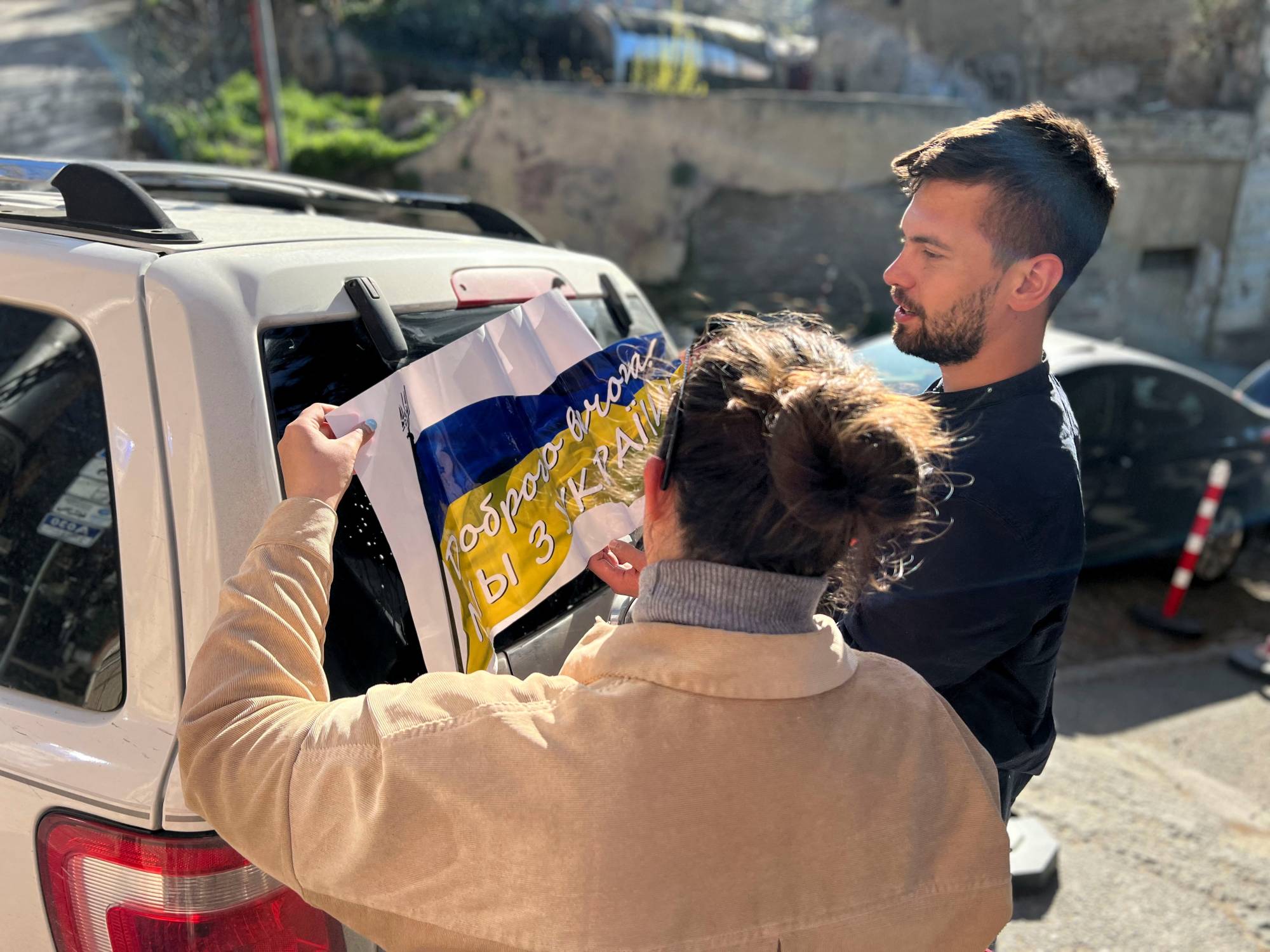 Maria Belkina and her partner Kirill Zhivoi, co-founders of Volunteers Tbilisi, a group which helps refugees from Ukraine, stick a sign with the Ukrainian flag onto a vehicle in Tbilisi, Georgia, on April 15. | Maria Belkina / via REUTERS