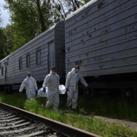 Ukrainian forensics experts carry the body of a Russian soldier exhumed in the village of Zavalivka, west of Kyiv, before it is stored in a refrigerated rail car stacked with Russian war dead on Wednesday. | AFP-JIJI