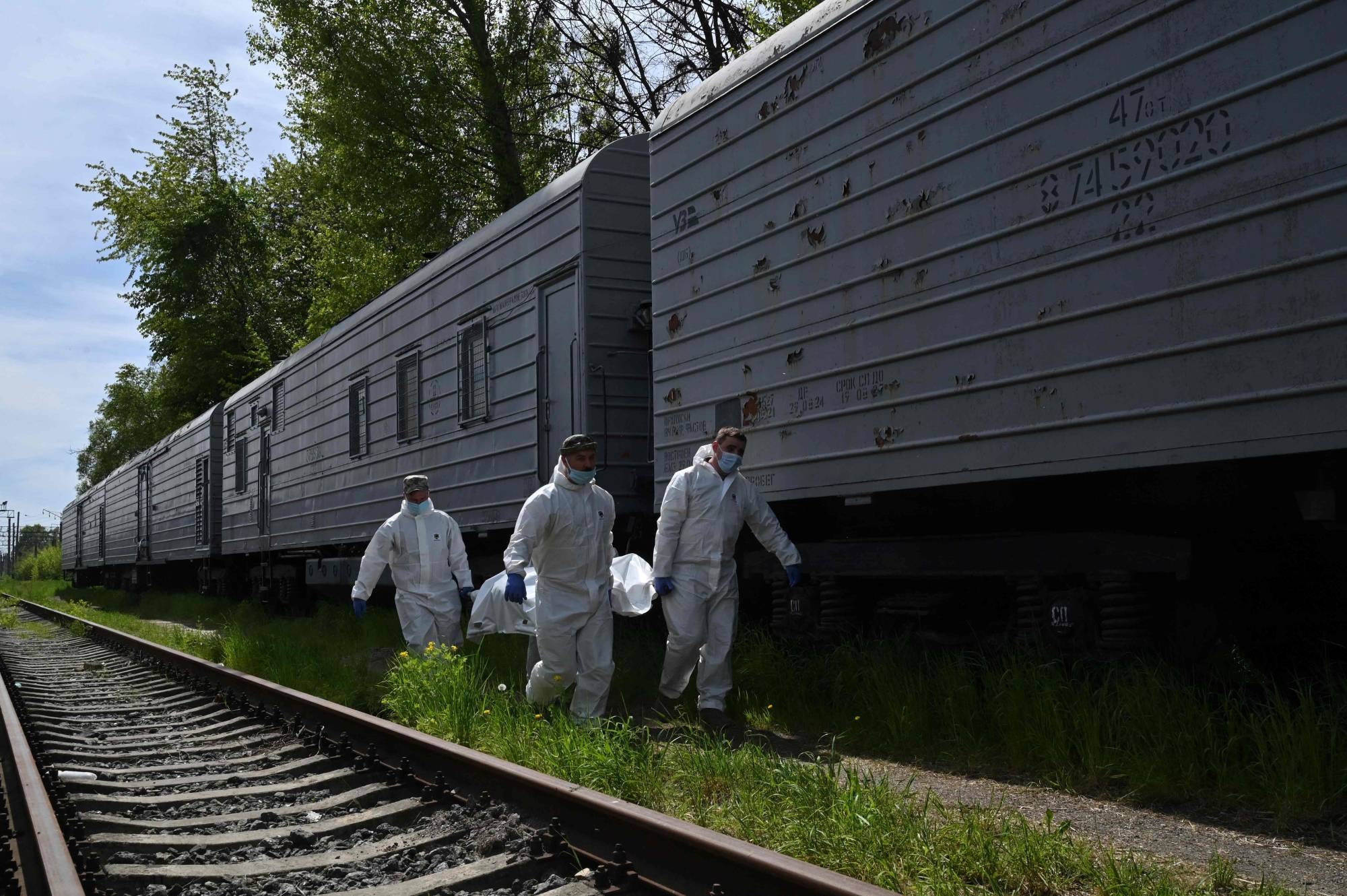 Ukrainian forensics experts carry the body of a Russian soldier exhumed in the village of Zavalivka, west of Kyiv, before it is stored in a refrigerated rail car stacked with Russian war dead on Wednesday. | AFP-JIJI